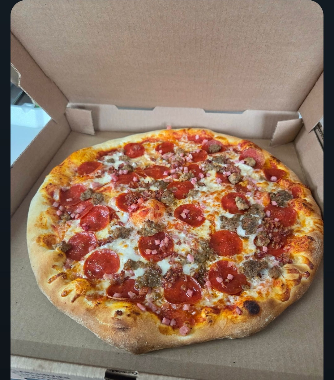 A loaded meat pizza with pepperoni, sausage and ham in a box