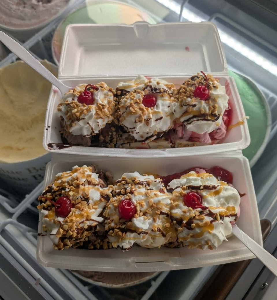 Two banana splits loaded with whipped cream, nuts and cherries